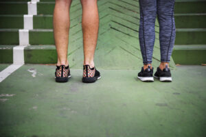 Two people standing on a green court showing foot alignment differences, illustrating overpronation and supination.