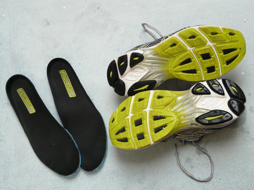 Running shoes with removable insoles displayed on a light surface — showing lime green and black treaded soles and cushioned inserts, representing athletic footwear design and comfort technology.