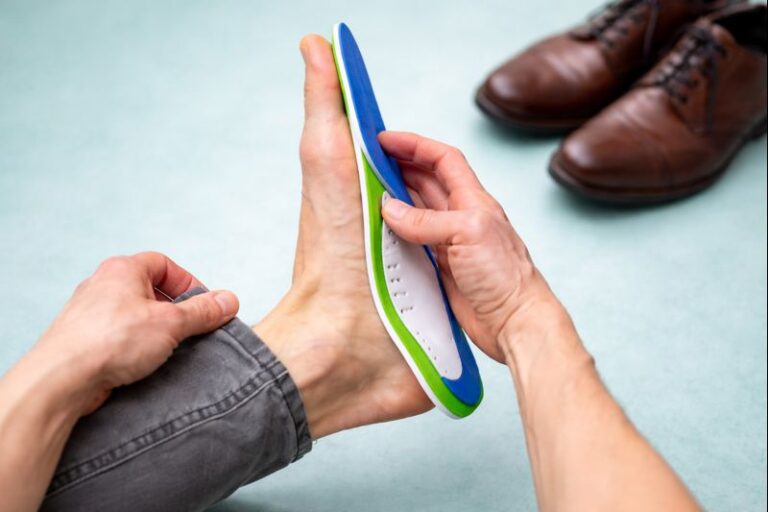 Close up of man hands fitting orthopedic insoles on a gray background