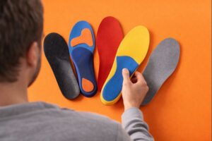 Person comparing different custom insoles on an orange background, selecting the right insole for comfort, support, and foot alignment